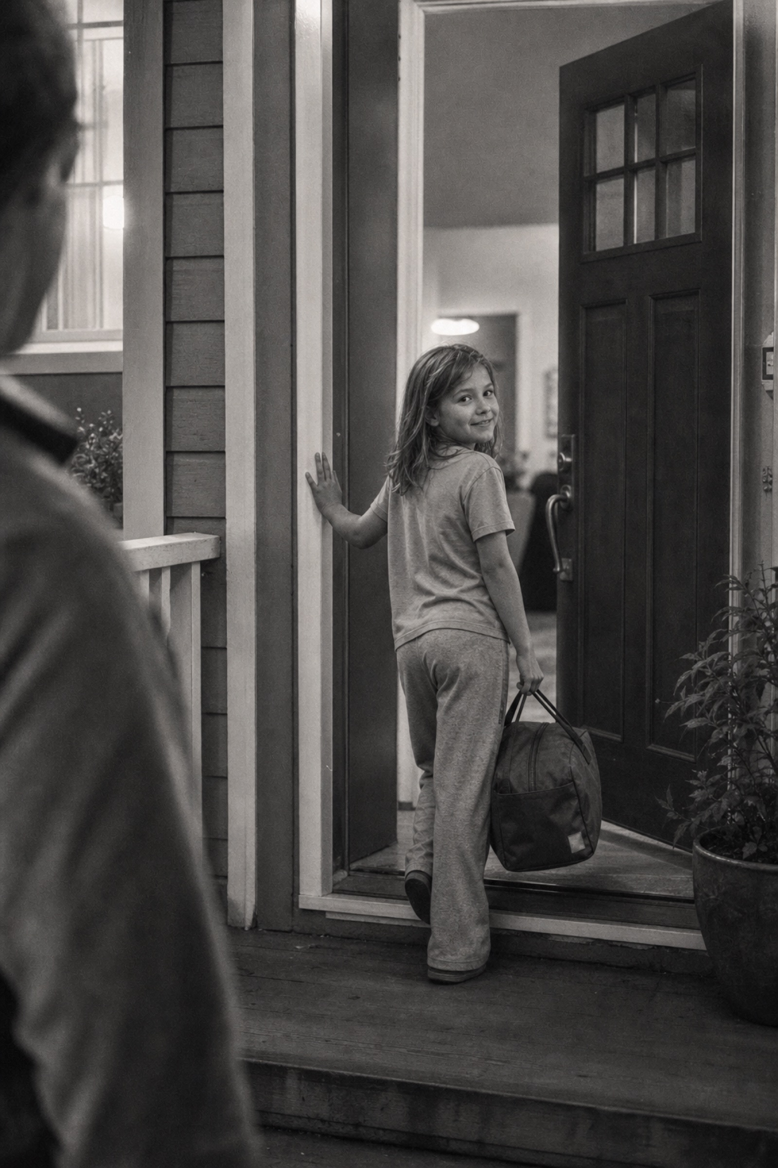 A child with an overnight bag stepping through a friend's front door, glancing back with a small smile